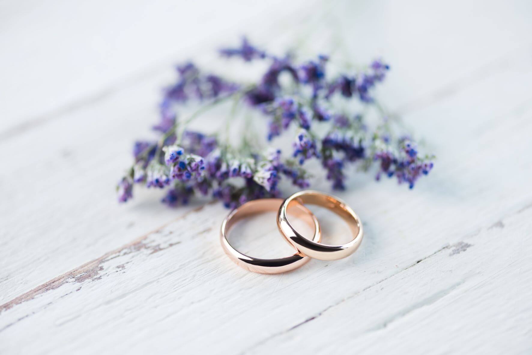 Two wedding rings with purple flowers behind